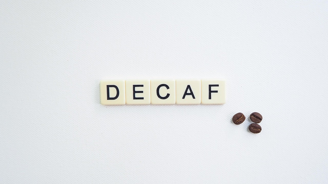 Aus Buchstabensteinen zusammengesetztes Wort "DECAF", entkoffeiniert. Es werden drei Kaffeebohnen abgebildet.