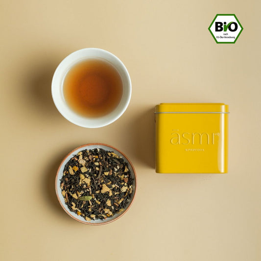 āsmi Ayurveda Ashwagandha Kurkuma Tee für Energie mit Bio-Siegel in gelber Dose und Tasse Tee