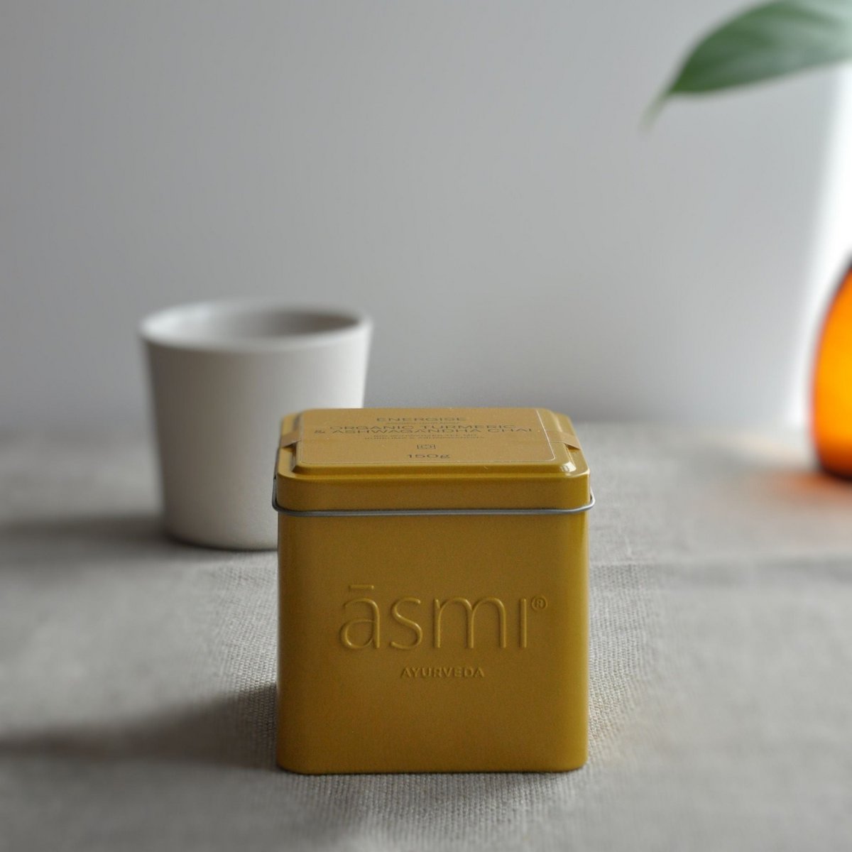 āsmi Ayurveda Ashwagandha Kurkuma Tee für Energie in gelber Metallbox auf grauem Tisch