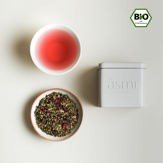 āsmi Ayurveda heiliger basilikum tee bio mit losem Tee, aufgebrühtem Tee in Tasse und weißer Dose